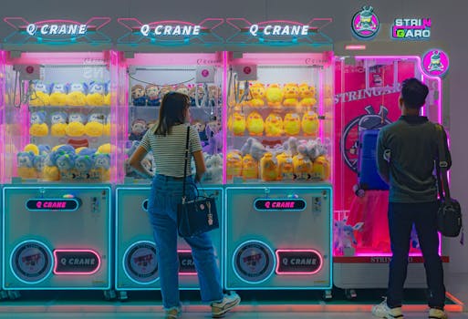 Two young adults engaging with vibrant claw machines filled with plush toys.